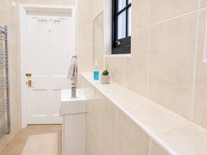 Une salle de bain avec une porte blanche, un lavabo, un porte-serviettes, une fenêtre et une petite plante posée sur le comptoir.