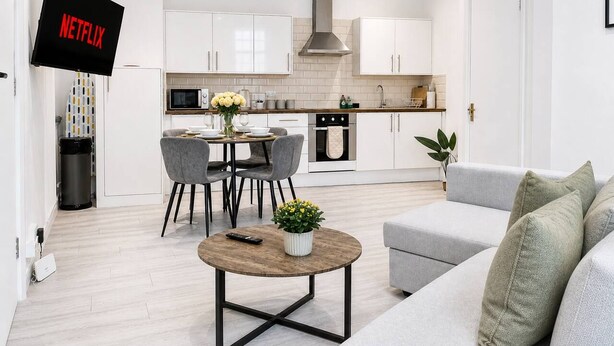Cozinha moderna com armários brancos, uma ilha central e um espaço de jantar com cadeiras e mesa.