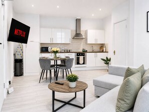 A modern kitchen with white cabinets, a central island, and a dining area with chairs and a table.