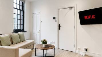 A modern living room with a sofa, a coffee table, a potted plant, and a wall-mounted TV displaying the Netflix logo.
