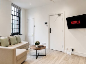 A modern living room with a sofa, a coffee table, a potted plant, and a wall-mounted TV displaying the Netflix logo.