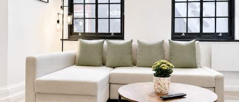 Un salon moderne avec un canapé d’angle, une table basse ronde et une plante en pot.