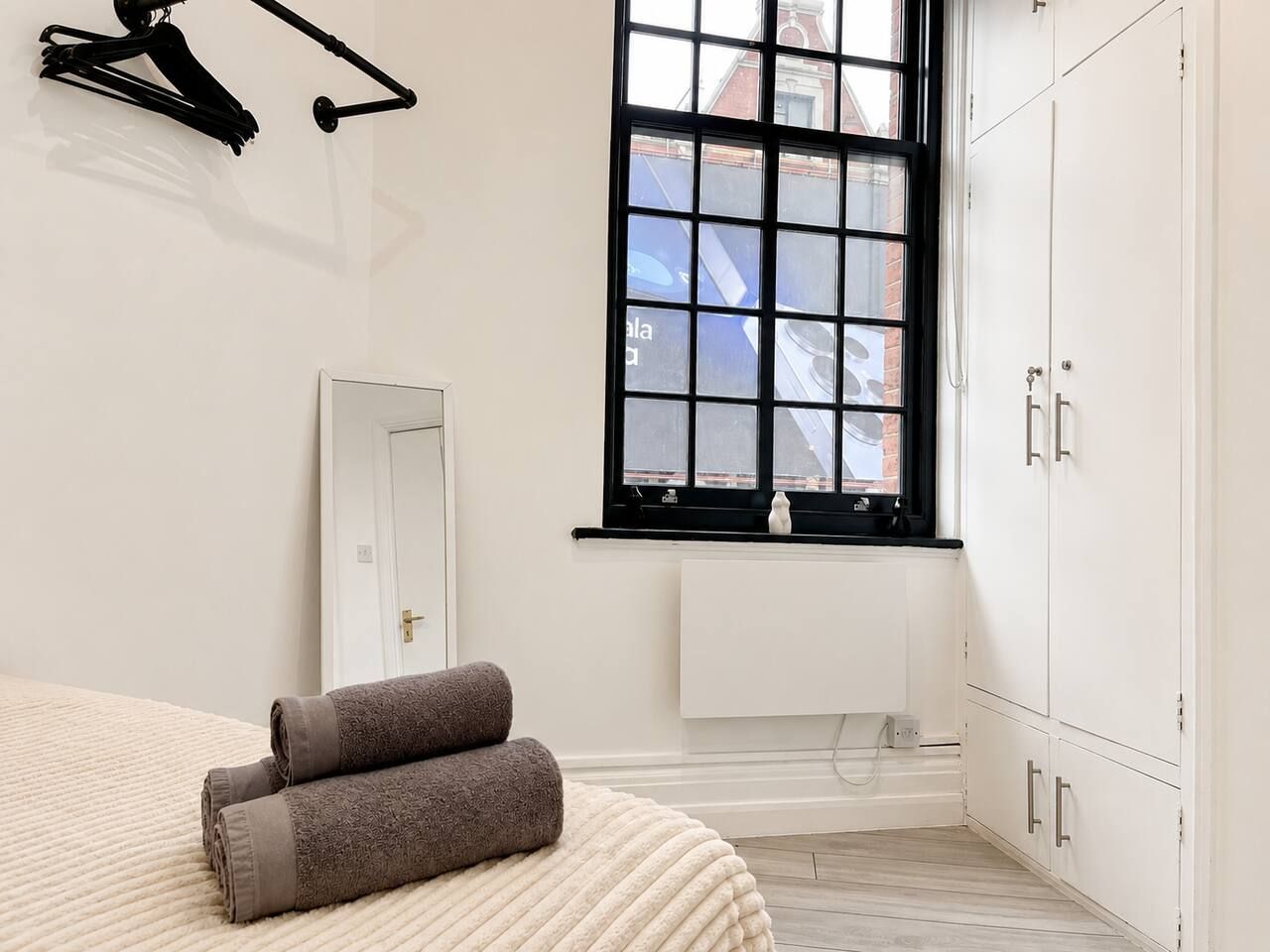 A bedroom with a bed, a window, a radiator, and a wardrobe.