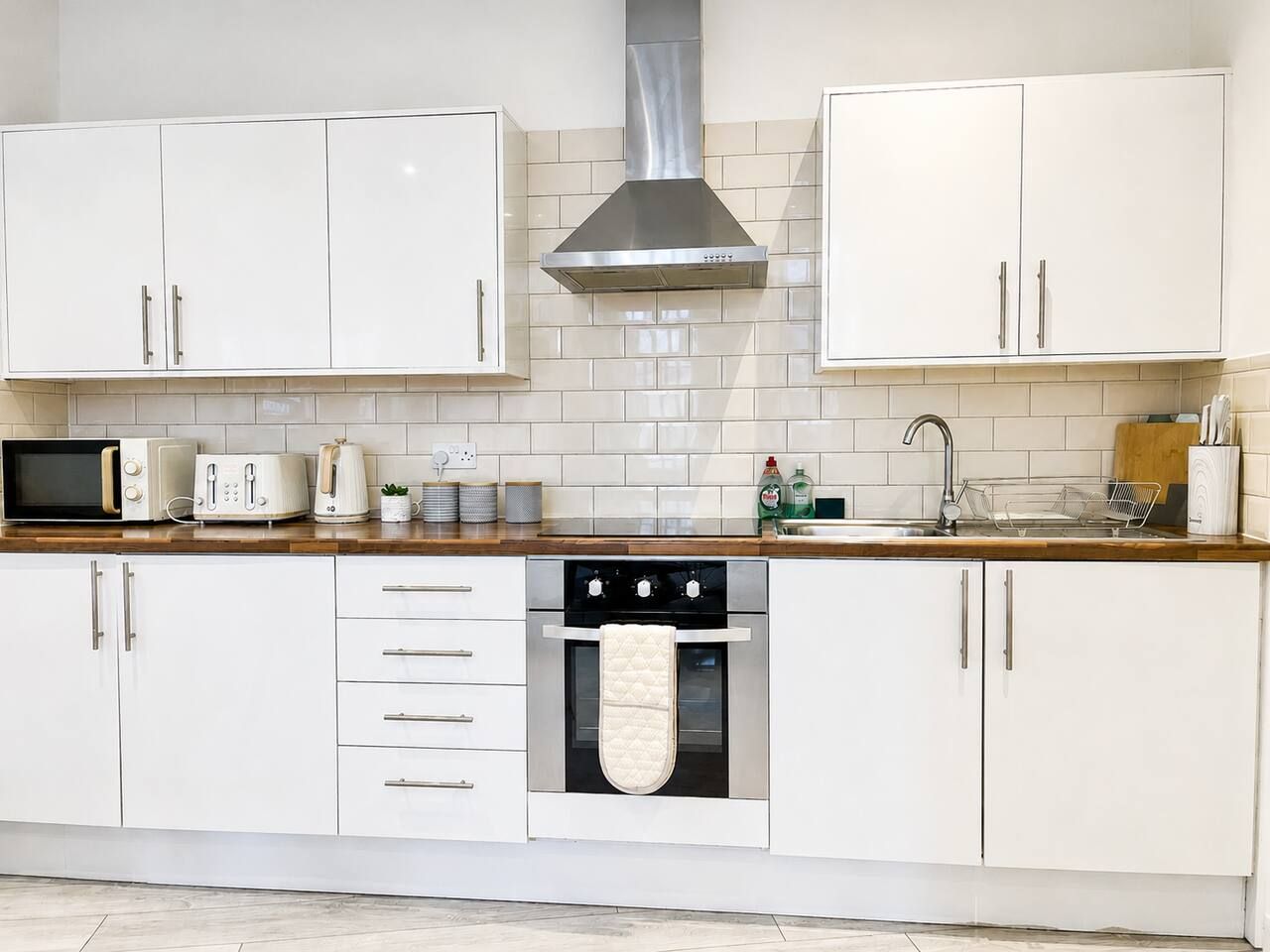 A modern kitchen with white cabinets, a stainless steel range hood, a microwave, toaster, and a kettle.