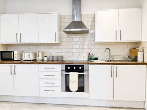 Une cuisine moderne avec des meubles blancs, une hotte en acier inoxydable, un four à micro-ondes, un grille-pain et une bouilloire.