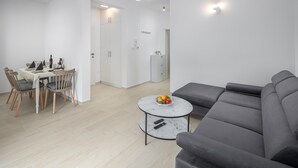 A modern living room with a grey sofa, a round coffee table with fruit, and a dining area with a table set for four. - Awesome apartment in Porec with WiFi (Porec)