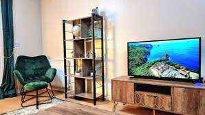 Ein Wohnzimmer mit einem grünen Sessel, einem Holz-Fernsehschrank und einem Bücherregal.