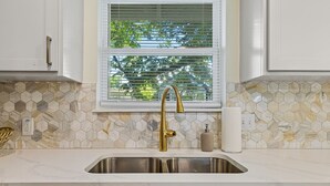 Eine Küche mit Spüle aus Edelstahl, weißen Schränken, einem Wasserhahn in Goldfarbe und einem Fenster mit Jalousien.