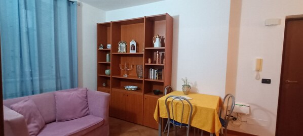 A living room with a pink sofa, a wooden bookshelf, and a small table with a yellow tablecloth.