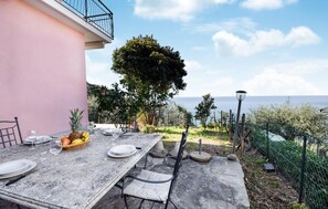 An outdoor dining area with a table set for four, surrounded by chairs, a basket of fruit, and a view of the sea. - Amazing home in Moneglia with WiFi (Moneglia)