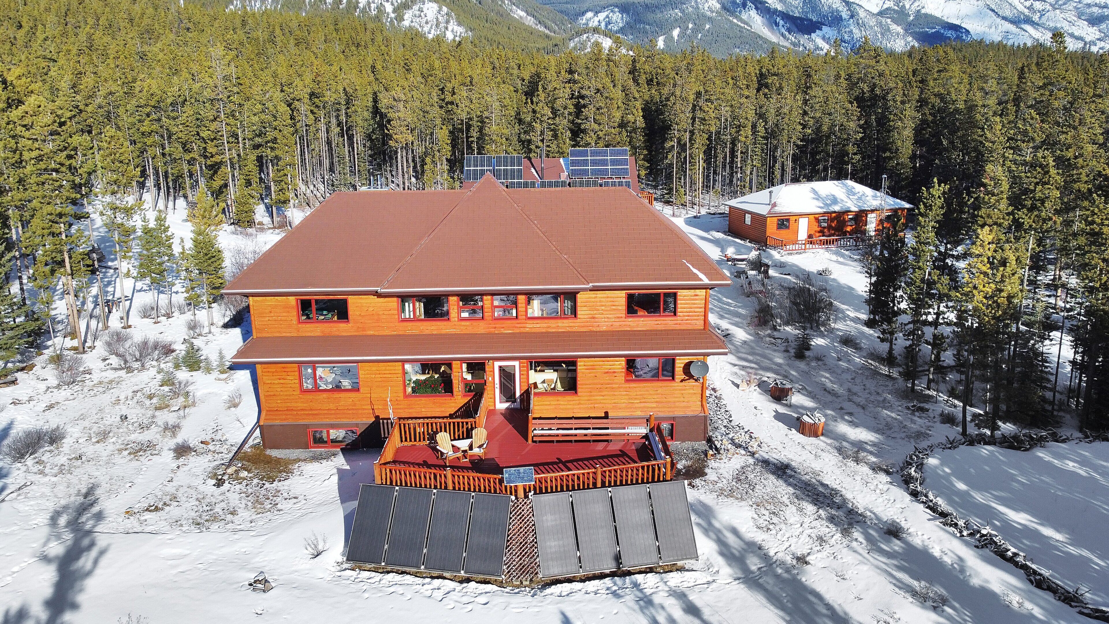 A two-story wooden cabin with a red roof, surrounded by a snowy landscape and a forest.