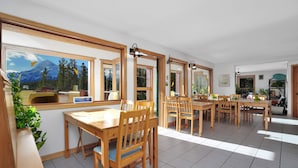 A spacious dining area with wooden tables and chairs, large windows with mountain views, and a bright, well-lit interior. - Aurum Lodge (Cline River)