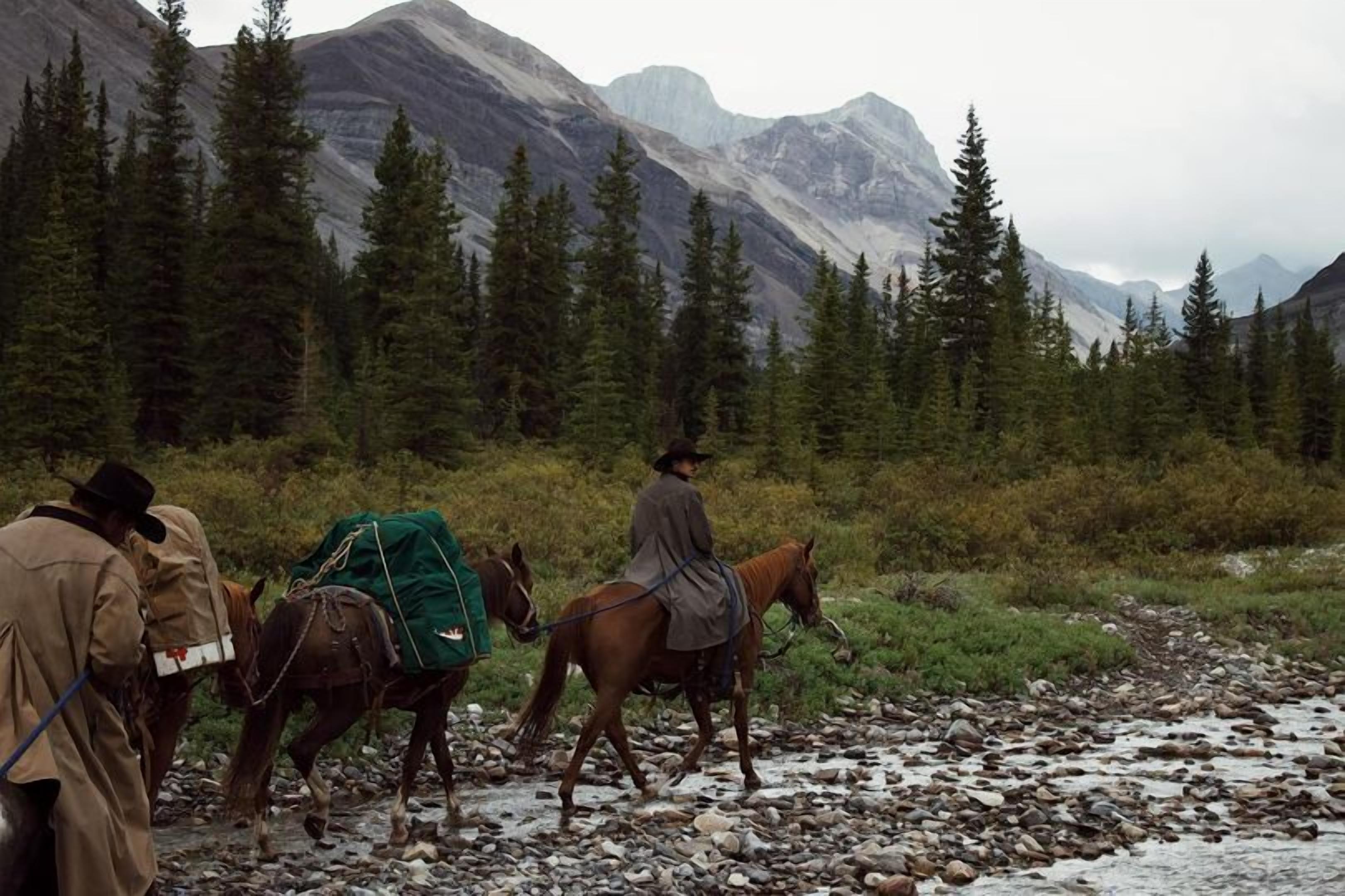 A group of people on horseback in a mountainous area with rocky terrain and dense forests.