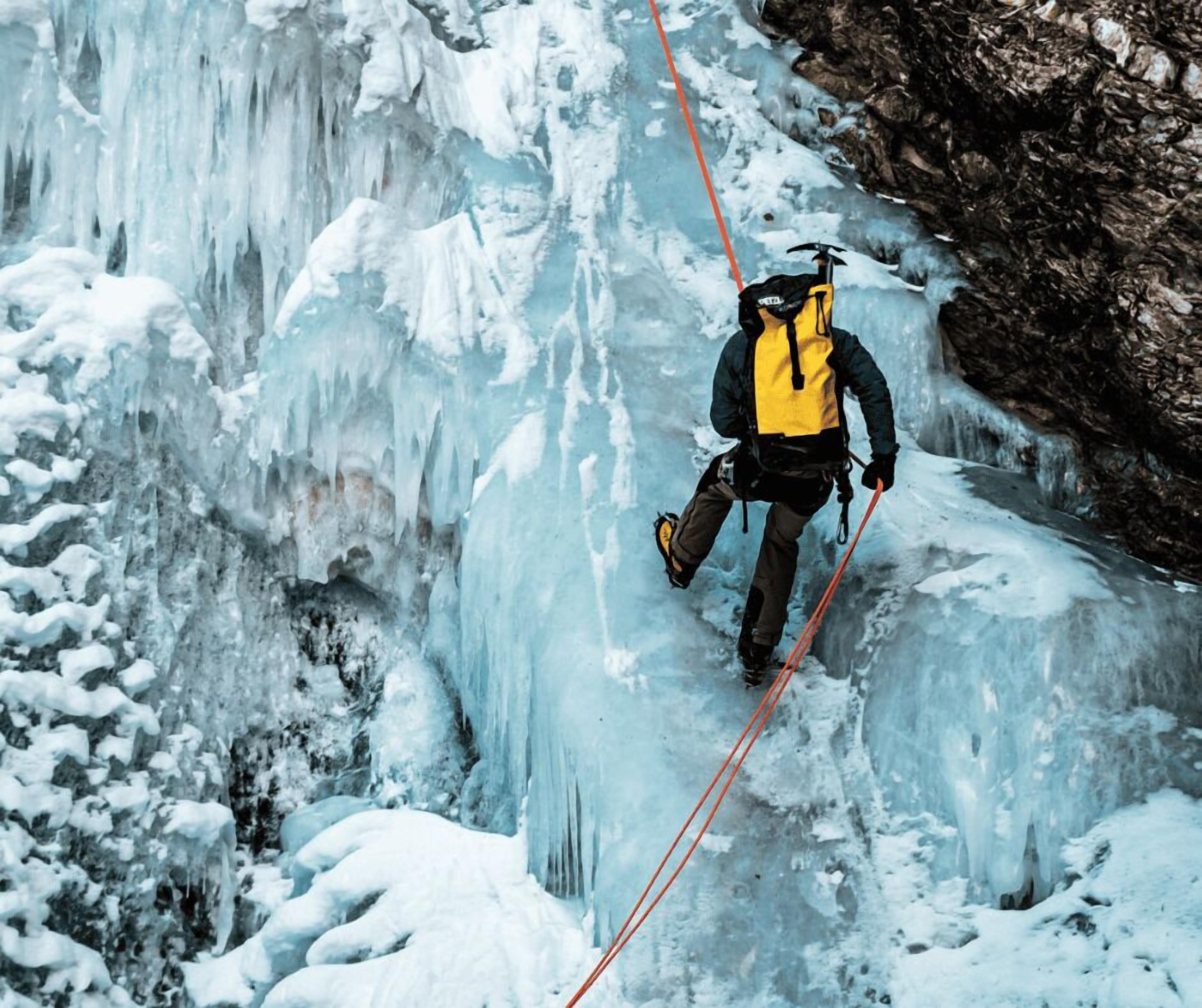 Une personne qui descend en rappel une falaise enneigée et glacée, à l’aide d’un harnais et de cordes.