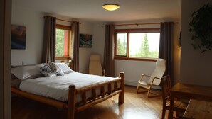 A bedroom with a wooden bed, a chair, a table, and a window with curtains. - Aurum Lodge (Cline River)
