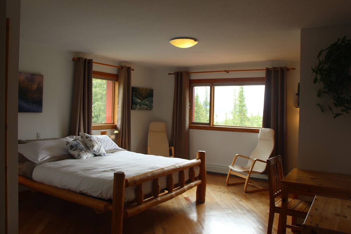 A bedroom with a wooden bed, a chair, a table, and a window with curtains.