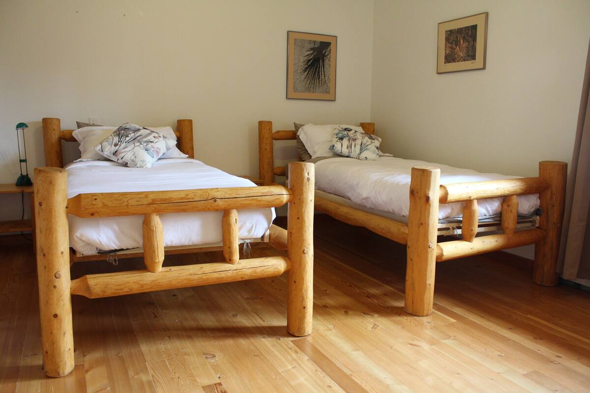 Two wooden bunk beds with white bedding, a wooden floor, and two framed pictures on the wall.