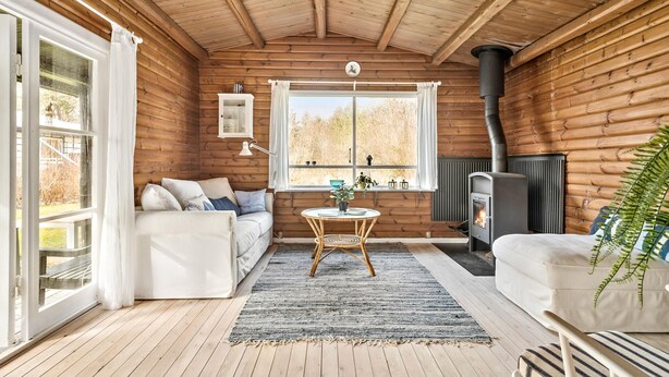 A cozy cabin interior with a sofa, a small round table, a window with curtains, a fireplace, and a plant. - Beautiful home in Frederiksværk (Frederiksværk)