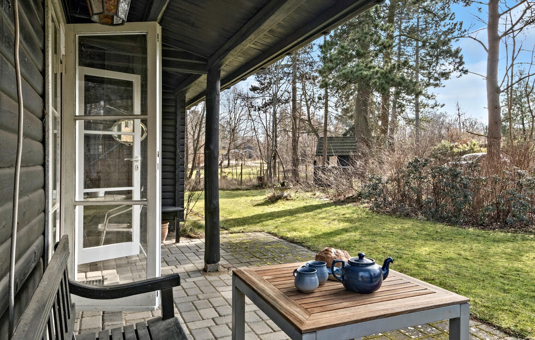 A wooden table with teapots and a bench outside a house with a glass door.