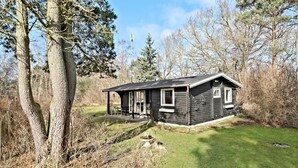 A small cabin with a porch, surrounded by trees and a grassy area. - Beautiful home in Frederiksværk (Frederiksværk)