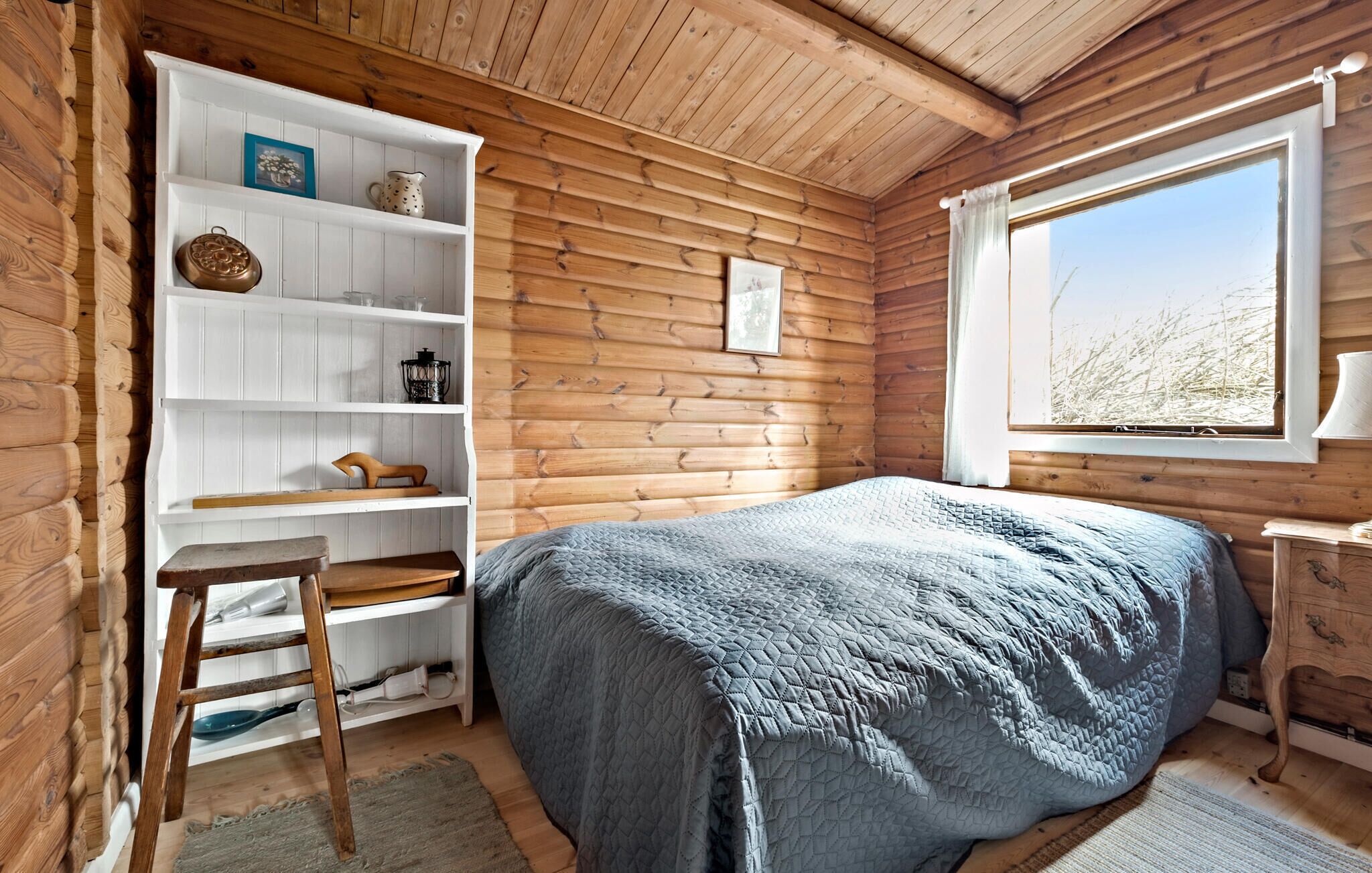 Um quarto de cabana acolhedor, com uma cama, uma estante de madeira, uma escrivaninha e uma janela com vista para o exterior.