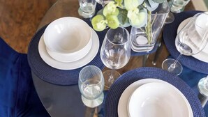 Une table dressée avec de l’argenterie blanche, des serviettes bleues et des verres à vin transparents, et un vase rempli de feuilles vertes en arrière-plan.