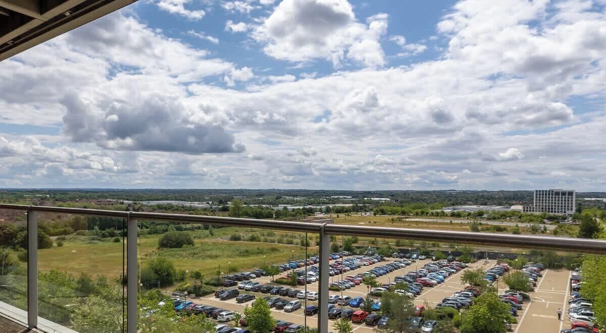 A parking lot with multiple rows of cars, a grassy area, and a building in the background.