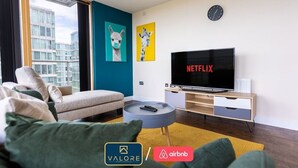 Un salon moderne avec un canapé, une table basse, un téléviseur et des œuvres d’art accrochées au mur.