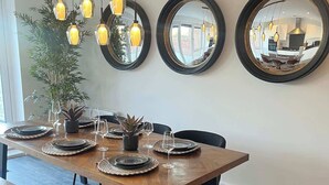 A dining area with a wooden table set for four, surrounded by chairs. Above the table, there are three hanging pendant lights and three round mirrors on the wall.