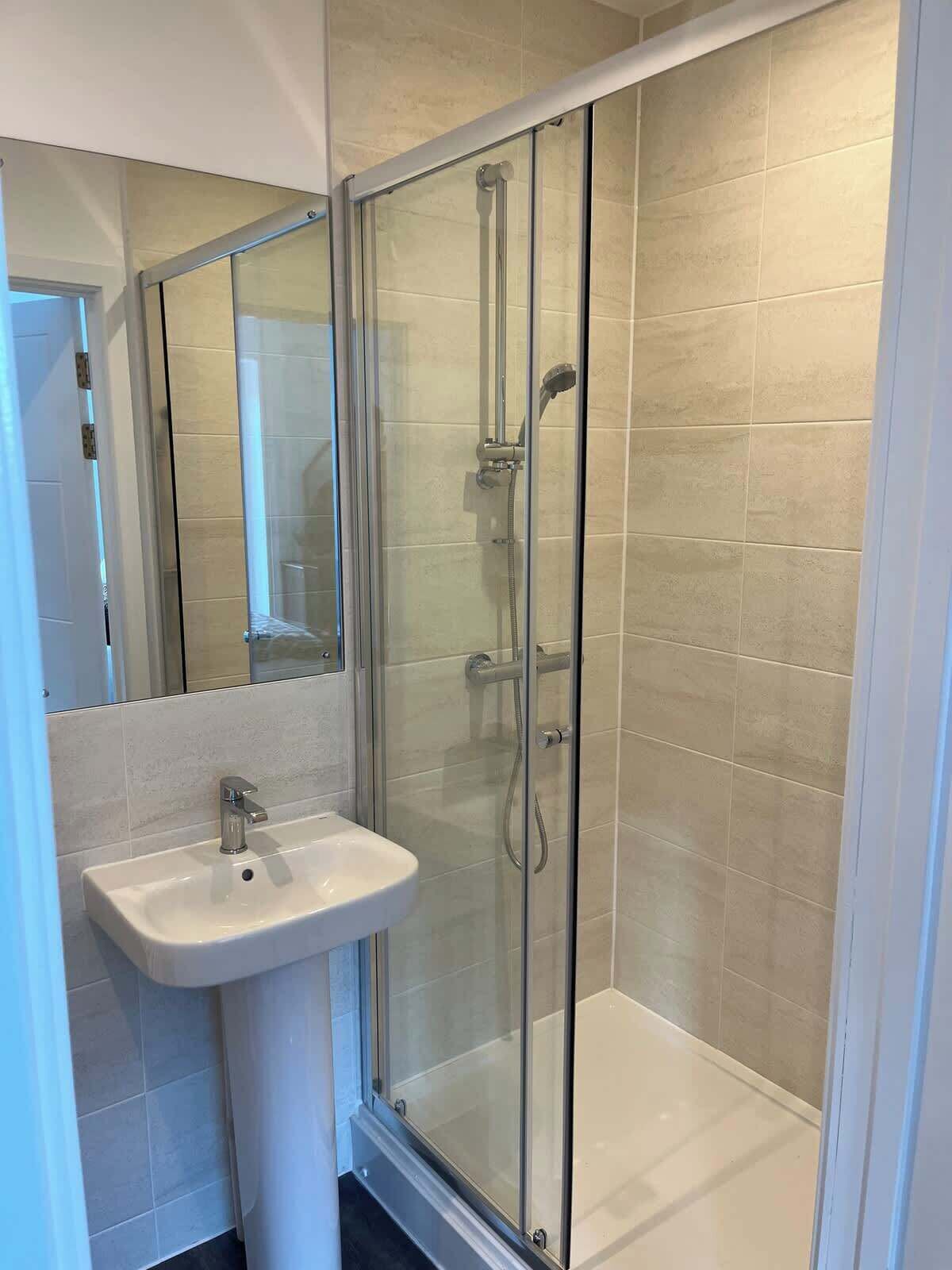 A modern bathroom with a glass-enclosed shower, a white pedestal sink, and beige tiled walls.