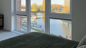 A bedroom with a large window overlooking a river and a bridge.