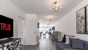 A modern living room with a flat-screen TV, a sofa, patterned cushions, and a dining area with chairs and a table. - 5-Bed Home | Canal Views | Parking for 2+ Cars (Milton Keynes)