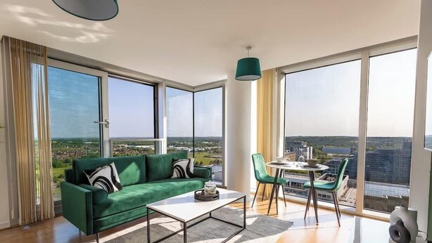 Ett modernt vardagsrum med en grön soffa, ett soffbord och en matplats med stolar och ett bord. Stora fönster ger utsikt över stadsbilden.