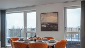 A dining area with a table set for six, large windows, and a painting on the wall.