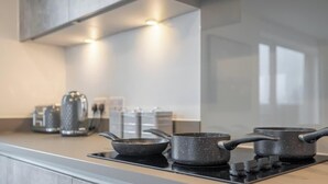 A modern kitchen with a gas stove, two frying pans, and a kettle.