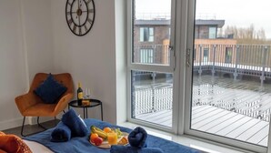 A room with a bed, a chair, a small table with a bottle and glasses, and a breakfast tray with fruits and juice.