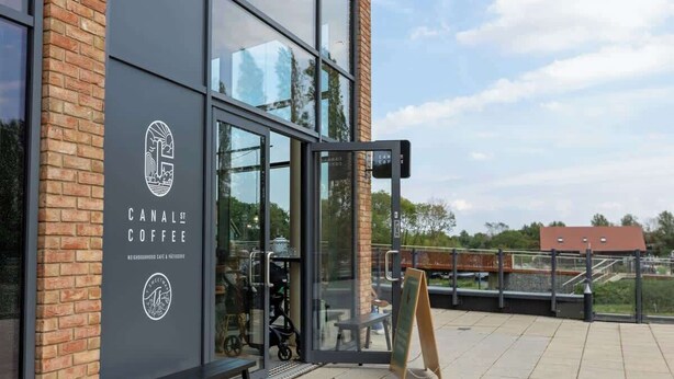 A modern coffee shop with a glass facade, a bench outside, and a chalkboard menu.