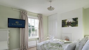 Une chambre à coucher comprenant un lit, une télévision, une fenêtre avec des rideaux, une cheminée et un tableau accroché au mur.