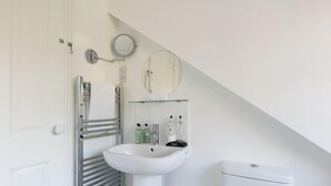 Une salle de bain moderne avec un lavabo blanc, une étagère en verre où sont rangés les articles de toilette, un miroir rond et un porte-serviettes.