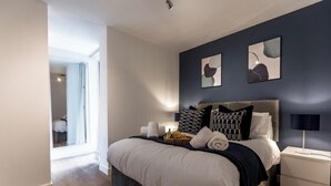 Een moderne slaapkamer met een groot bed, een nachtkastje en een bedtafel. Boven het bed hangen abstracte kunstwerken.