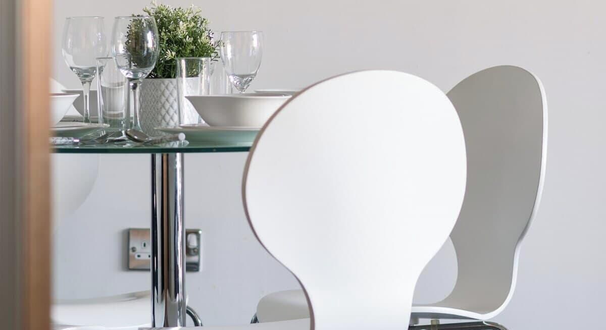 Zona pranzo moderna con tavolo in vetro, sedie bianche e una piccola pianta in vaso.