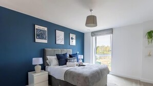Een moderne slaapkamer met een groot bed, een nachtkastje en een raam met uitzicht op de omgeving.