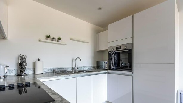 Een moderne keuken met witte kasten, een zwart aanrecht, een inbouwoven en een roestvrijstalen spoelbak.