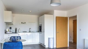 Een moderne keuken met witte kasten, een marmeren aanrecht en een eethoek met een blauwe tafelkleed.