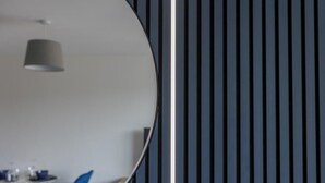Een modern interieur met een ronde spiegel die een plafondlamp weerspiegelt en een blauwe stoel.