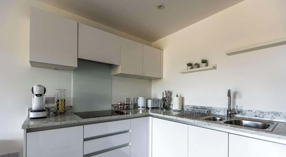 Una cocina moderna con armarios blancos, un lavamanos de acero inoxidable y una encimera de mármol.