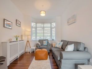 Uma sala de estar moderna com um sofá cinzento, um banquinho castanho, um radiador branco e uma janela com persianas.