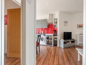 Une cuisine moderne avec des carreaux rouges, un lave-linge et un téléviseur dans un espace de vie compact.