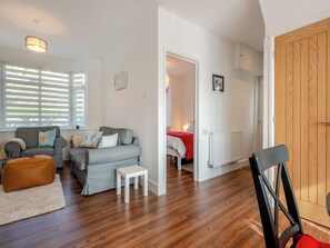 A modern living room with a grey sofa, a small white table, and a brown ottoman. There is a wooden door and a radiator on the wall. - 2 bedroom accommodation in Goodwick (Goodwick)