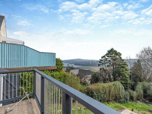 A balcony with a view of a lake, a wooden deck, and a blue building in the background. - 2 bedroom accommodation in Goodwick (Goodwick)